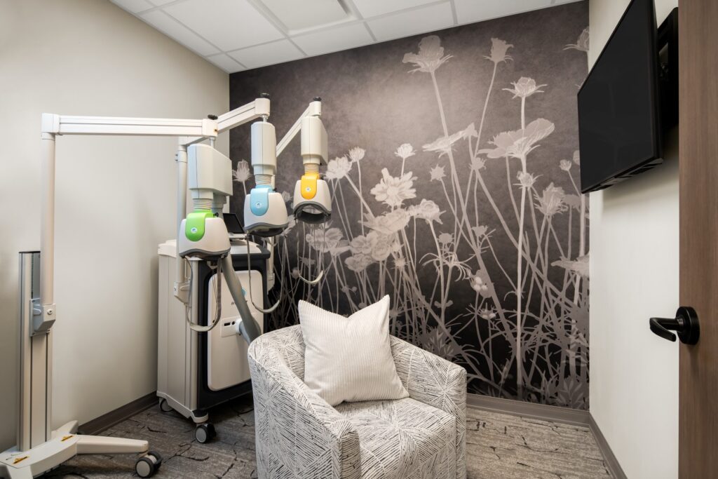 Treatment room with medical equipment for detox services, featuring a cozy seating area and floral wallpaper, emphasizing a calming environment for recovery support.