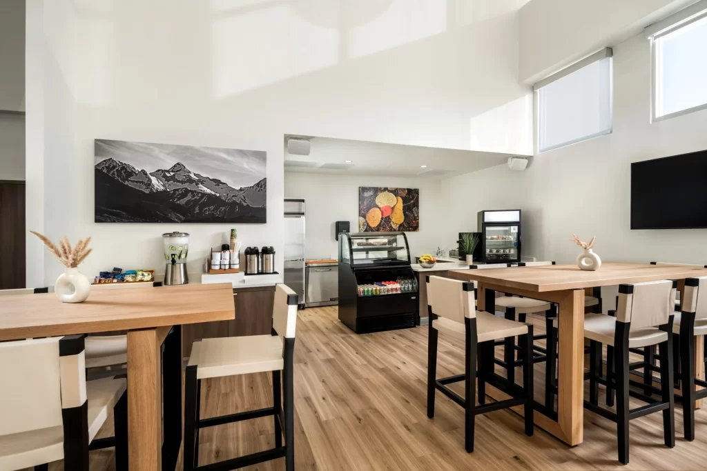 Modern cafe interior with two wooden tables, high chairs, coffee station, and artwork, creating a welcoming atmosphere for clients at APN DFW mental health and addiction treatment center.