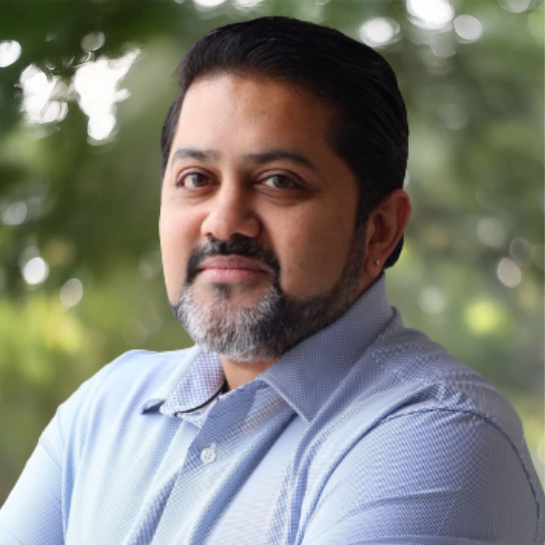 Dr. Manish Nair, MD, Medical Director at All Points North DFW, smiling with arms crossed, in a professional setting.